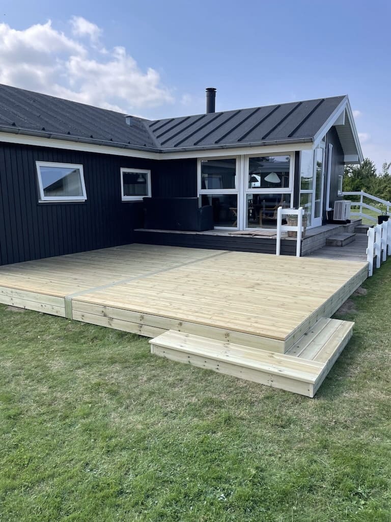 En komplet færdigbygget træterrasse med præcise udskæringer og en jævn overflade, der skaber en flot sammenhæng mellem boligen og haven